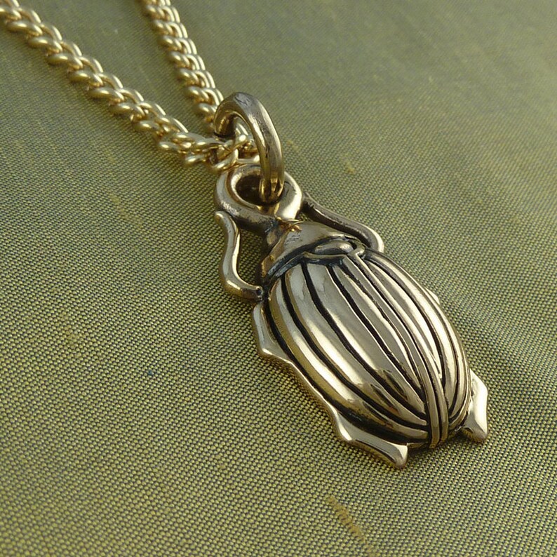 May include: A gold-toned beetle pendant necklace with a detailed design. The pendant is attached to a gold chain.