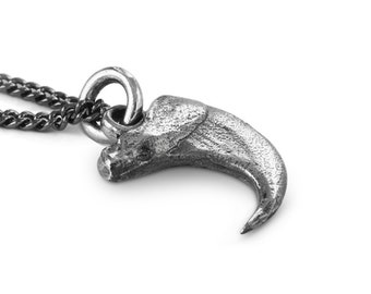 May include: A silver claw pendant necklace with a black chain. The claw is detailed and realistic, with a textured surface.