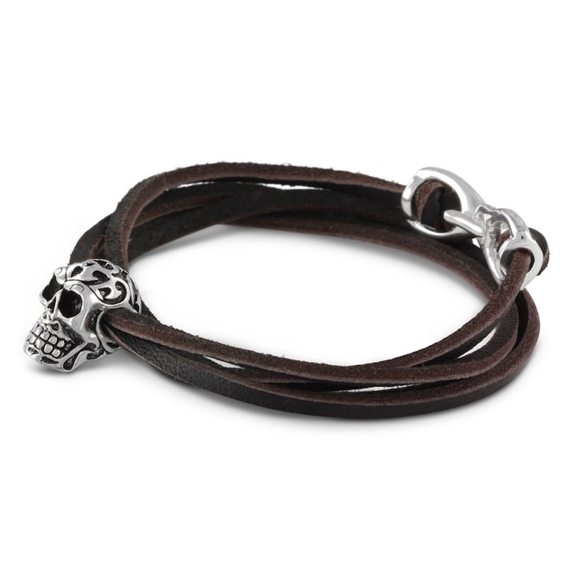 May include: A brown leather wrap bracelet with a silver skull charm. The bracelet has a silver clasp.