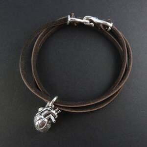 Pu&ograve; includere: Un braccialetto in pelle marrone con un ciondolo a forma di cuore anatomico in argento. Il braccialetto &egrave; avvolto due volte e ha una chiusura in argento.