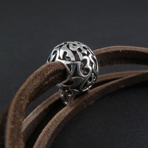 May include: A silver metal bead with an intricate floral design, threaded onto a brown leather cord.