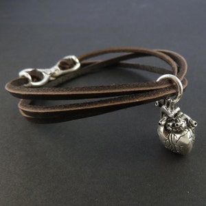 Pu&ograve; includere: Un braccialetto in pelle marrone con un ciondolo a forma di cuore anatomico argentato.