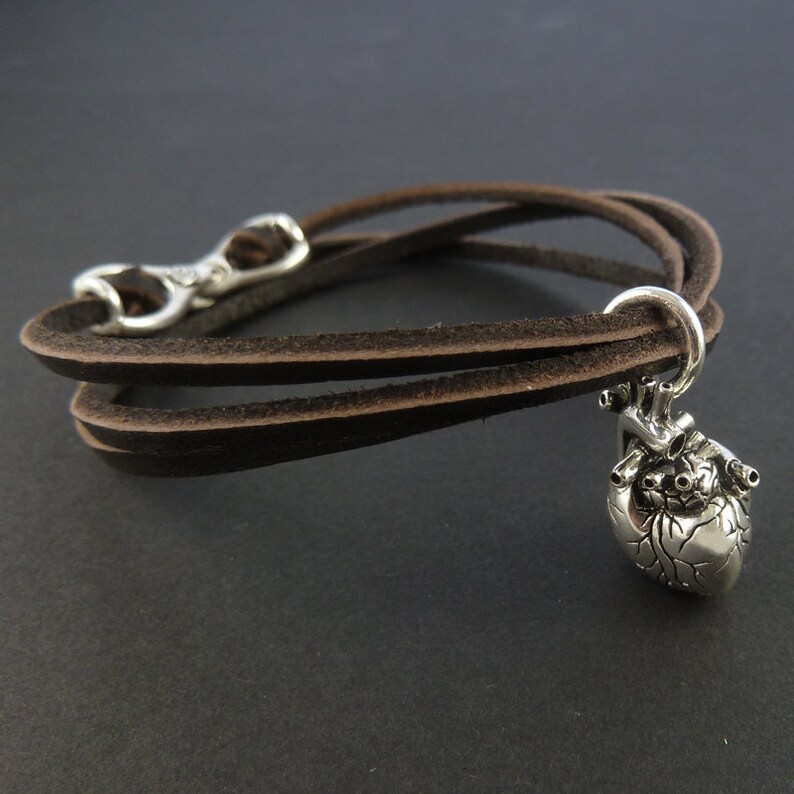 Pu&ograve; includere: Un braccialetto in pelle marrone con un ciondolo a forma di cuore anatomico argentato.