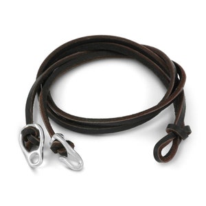 Puede incluir: Un brazalete de cuero marr&oacute;n con cierres de metal plateado. El brazalete est&aacute; hecho de una sola hebra de cuero que est&aacute; atada en un extremo con un nudo.