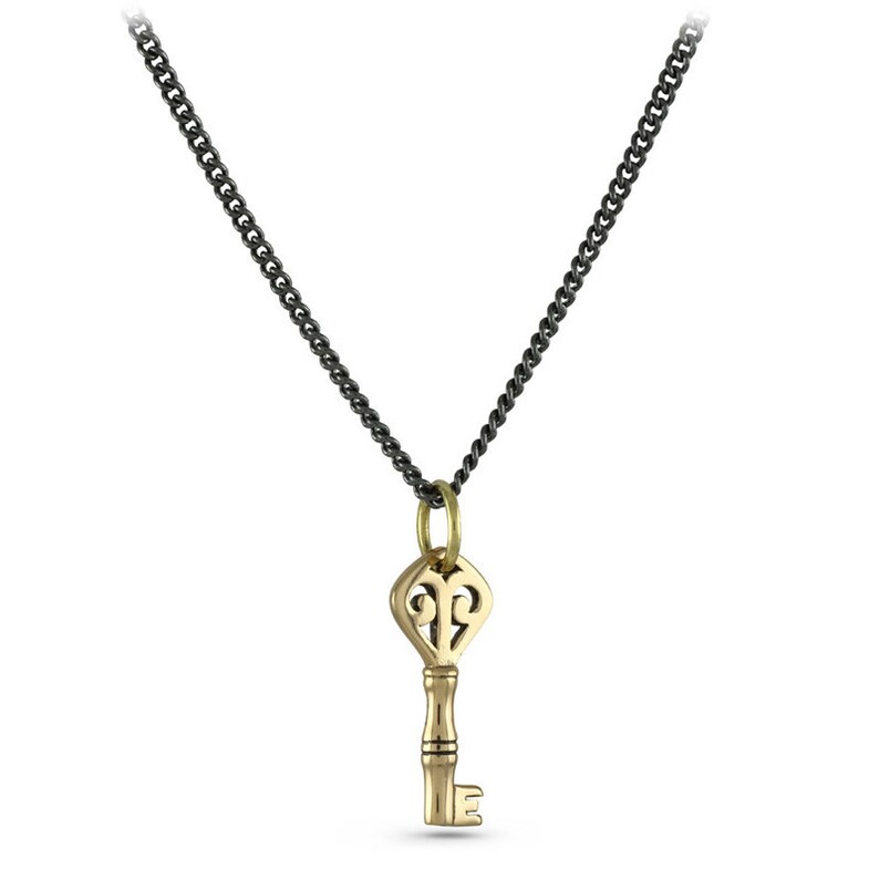 May include: A gold key pendant necklace with an ornate design on the key head. The necklace is on a black chain.