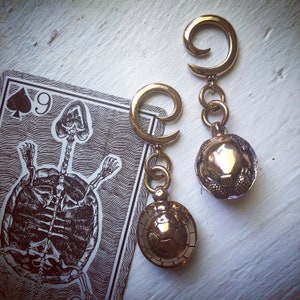 May include: Two gold-toned turtle-shaped earrings with a dangling design. The earrings are on a white surface.