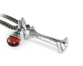 May include: Silver necklace with a bone pendant and a red gemstone. The bone pendant is detailed and realistic.