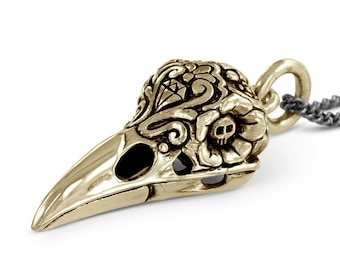 May include: Gold-toned pendant necklace featuring a detailed, ornate bird skull with floral accents. The skull has a small skull detail in the center of the floral design.