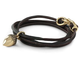 May include: A brown leather wrap bracelet with a gold acorn charm. The bracelet has a gold clasp.