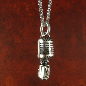 May include: A silver necklace with a vintage microphone pendant. The microphone has a detailed design with a silver finish.