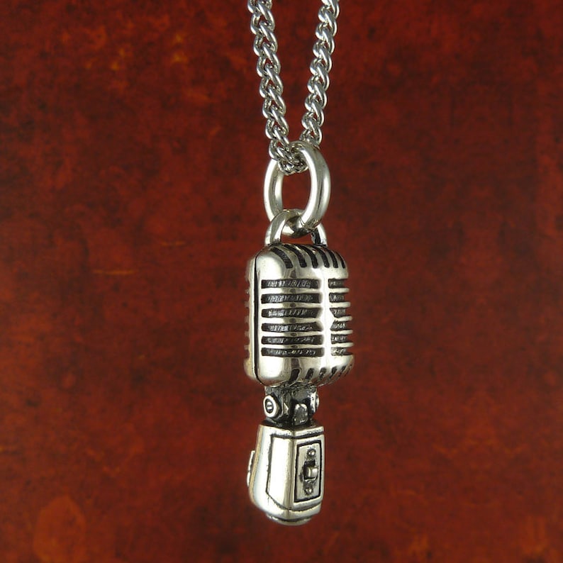 May include: A silver necklace with a vintage microphone pendant. The microphone has a detailed design with a silver finish.