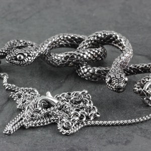 May include: A silver snake pendant necklace with a detailed snake design and a silver chain. The snake is coiled and has a textured surface.
