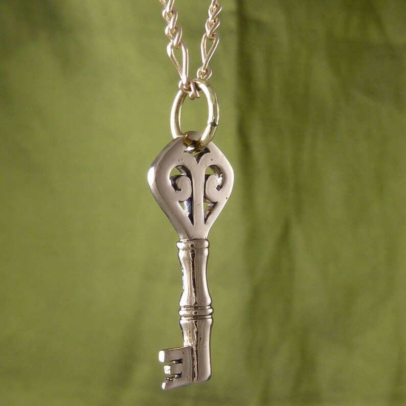 May include: A silver key pendant necklace with a decorative heart-shaped top and a detailed keyhole design. The necklace is on a gold chain.