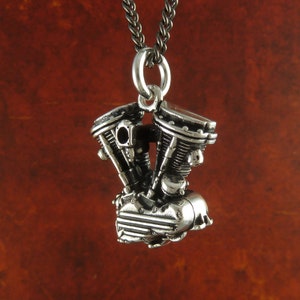 May include: Silver pendant necklace featuring a detailed miniature motorcycle engine. The pendant is attached to a silver chain.