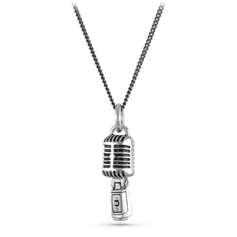 May include: A silver necklace with a vintage microphone pendant. The chain is black and the microphone is detailed with a silver finish.