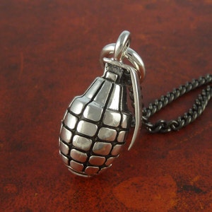 May include: A silver grenade pendant necklace with a black chain. The grenade is detailed with a textured surface and a pin.