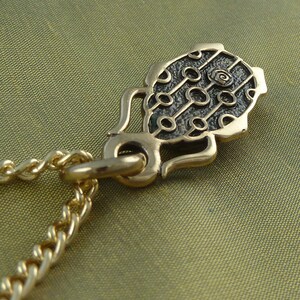May include: A gold chain necklace with a pendant featuring a black and green design with a circular pattern. The pendant is shaped like a stylized leaf.