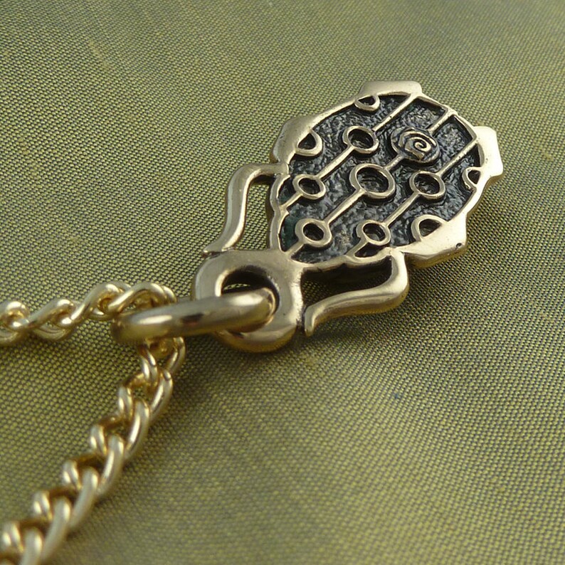 May include: A gold chain necklace with a pendant featuring a black and green design with a circular pattern. The pendant is shaped like a stylized leaf.