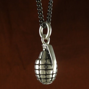 May include: A silver grenade pendant necklace with a black chain. The pendant is detailed with a textured surface and a ring at the top.