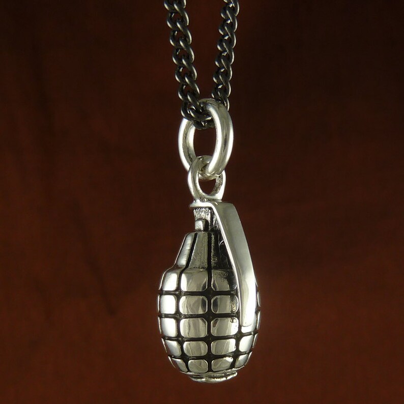 May include: A silver grenade pendant necklace with a black chain. The pendant is detailed with a textured surface and a ring at the top.