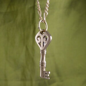 May include: A silver key pendant necklace with a decorative heart-shaped top and a gold chain.