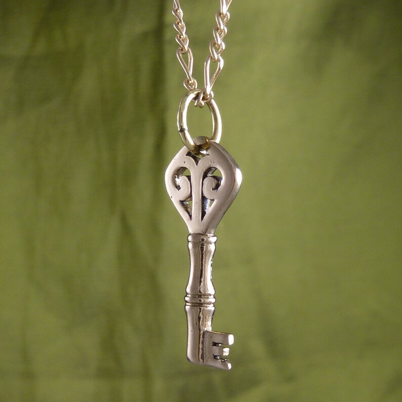 May include: A silver key pendant necklace with a decorative heart-shaped top and a gold chain.