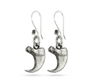 May include: A pair of silver earrings with a claw-shaped pendant. The claws are detailed and have a textured surface.