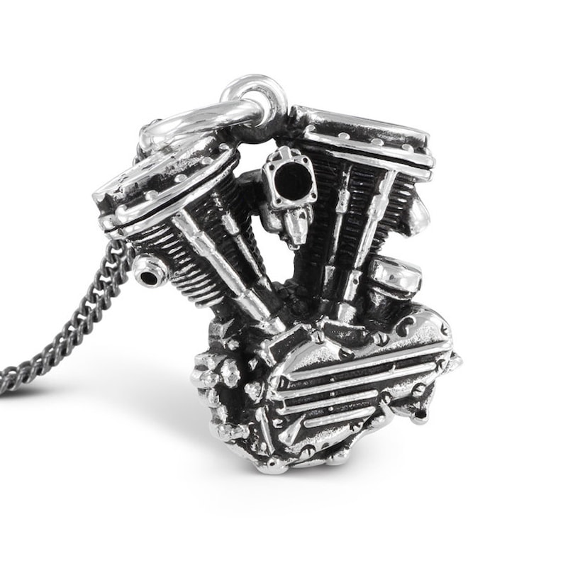 May include: A silver pendant necklace featuring a detailed miniature motorcycle engine. The pendant is attached to a silver chain.
