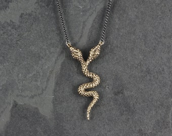 May include: A gold-toned double-headed snake pendant necklace on a black chain. The snake is coiled and has a textured surface.