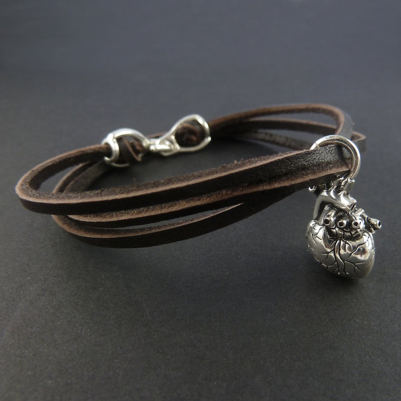 Pu&ograve; includere: Un braccialetto in pelle marrone con un ciondolo a forma di cuore anatomico argentato.