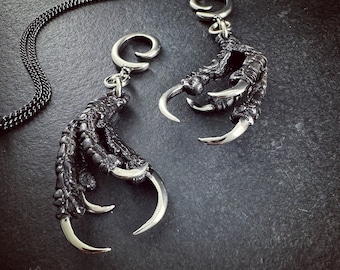 May include: Two silver claw-shaped pendants with detailed textured surfaces and sharp silver claws. The pendants are attached to silver chains.