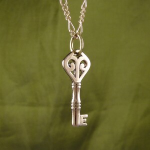 May include: A silver key pendant necklace with a decorative heart-shaped top and a chain.