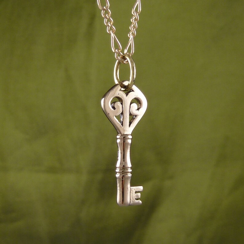 May include: A silver key pendant necklace with a decorative heart-shaped top and a chain.