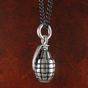 May include: A silver grenade pendant necklace with a black chain. The grenade is detailed with a textured surface.