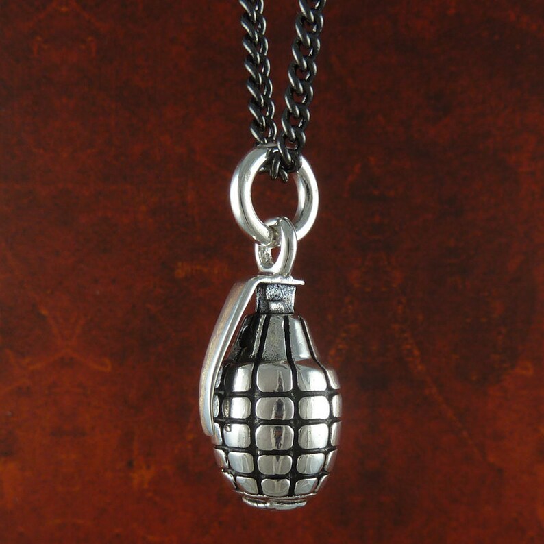 May include: A silver grenade pendant necklace with a black chain. The grenade is detailed with a textured surface.