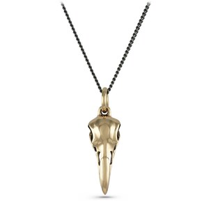 May include: A gold bird skull pendant necklace with a black chain.