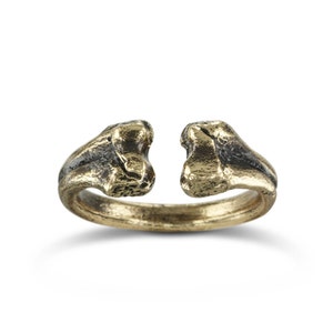 May include: A gold-toned ring with a unique, open design. The ring is made of two pieces that are joined together at the top, creating a gap in the middle. The ring has a rough, textured surface.