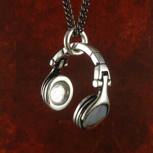 May include: A silver pendant necklace featuring a detailed design of a pair of headphones. The necklace is on a silver chain.