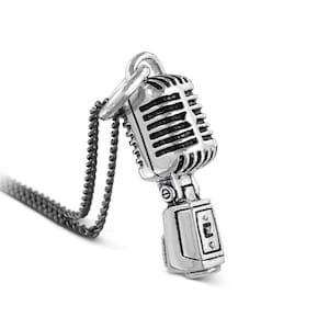 Op de afbeelding: Een zilveren ketting met een vintage microfoon hanger. De microfoon heeft een gedetailleerd ontwerp met een zwart rooster en een zilveren basis.