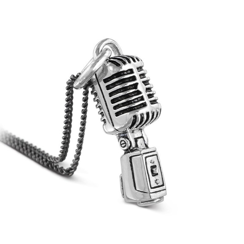 May include: A silver necklace with a vintage microphone pendant. The microphone has a detailed design with a black grille and a silver base.