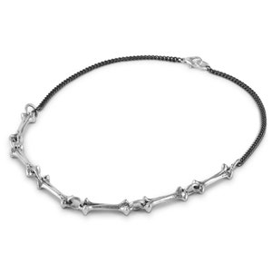 May include: A silver necklace with a chain made of small, linked bones. The chain is connected to a black chain with a clasp.