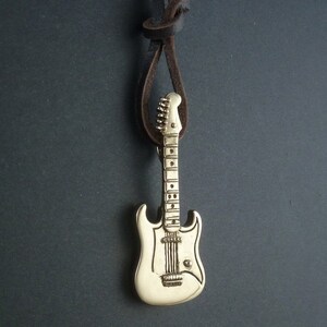 May include: A gold-colored electric guitar pendant on a brown leather cord. The guitar has a white body and a detailed fretboard.