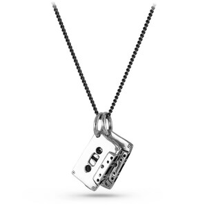 May include: A silver-toned pendant necklace featuring a detailed cassette tape design. The pendant hangs from a black beaded chain. The cassette tape pendant has intricate details, including the tape reels and the tape window.