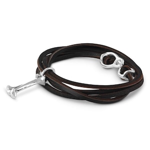 May include: A brown leather wrap bracelet with a silver bone charm. The bracelet is made of multiple strands of leather and has a silver clasp.