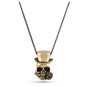 May include: A gold-toned skull pendant necklace with a top hat and a rose in its mouth. The necklace is on a black chain.