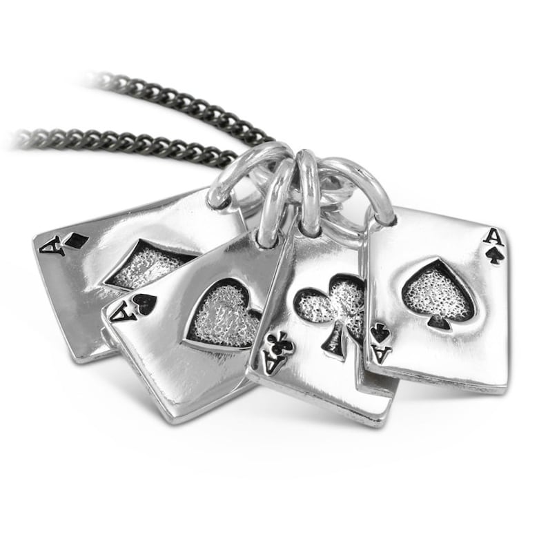 Puede incluir: Un collar de plata con un colgante que presenta cinco amuletos de cartas de juego de plata. Cada amuleto es un as con un palo diferente: picas, corazones, diamantes y tr&eacute;boles. El collar est&aacute; en una cadena negra.