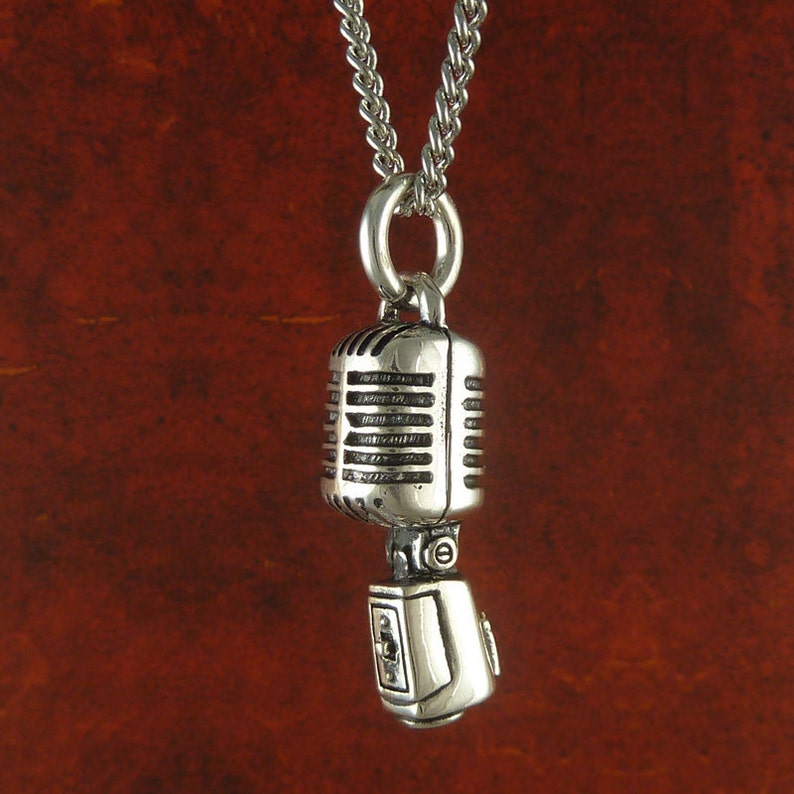 May include: Silver necklace with a vintage microphone pendant. The microphone is detailed with a silver finish and has a stand.