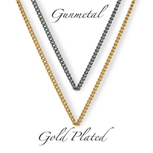 May include: Two chains, one gold plated and one gunmetal, are shown hanging against a white background. The chains are both curb chains.