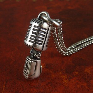 May include: A silver microphone pendant necklace with a detailed design. The microphone has a silver chain attached to it.