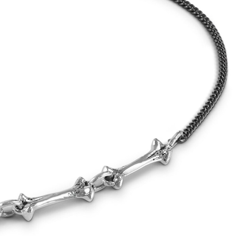May include: A silver necklace with a bone-shaped pendant. The chain is black and has a curb link design.